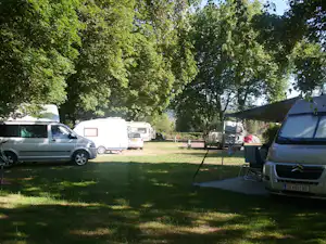 Campingplatz mit Stellplätzen, Autos und Wohnwagen sowie Zelten im Grünen zwischen Bäumen.