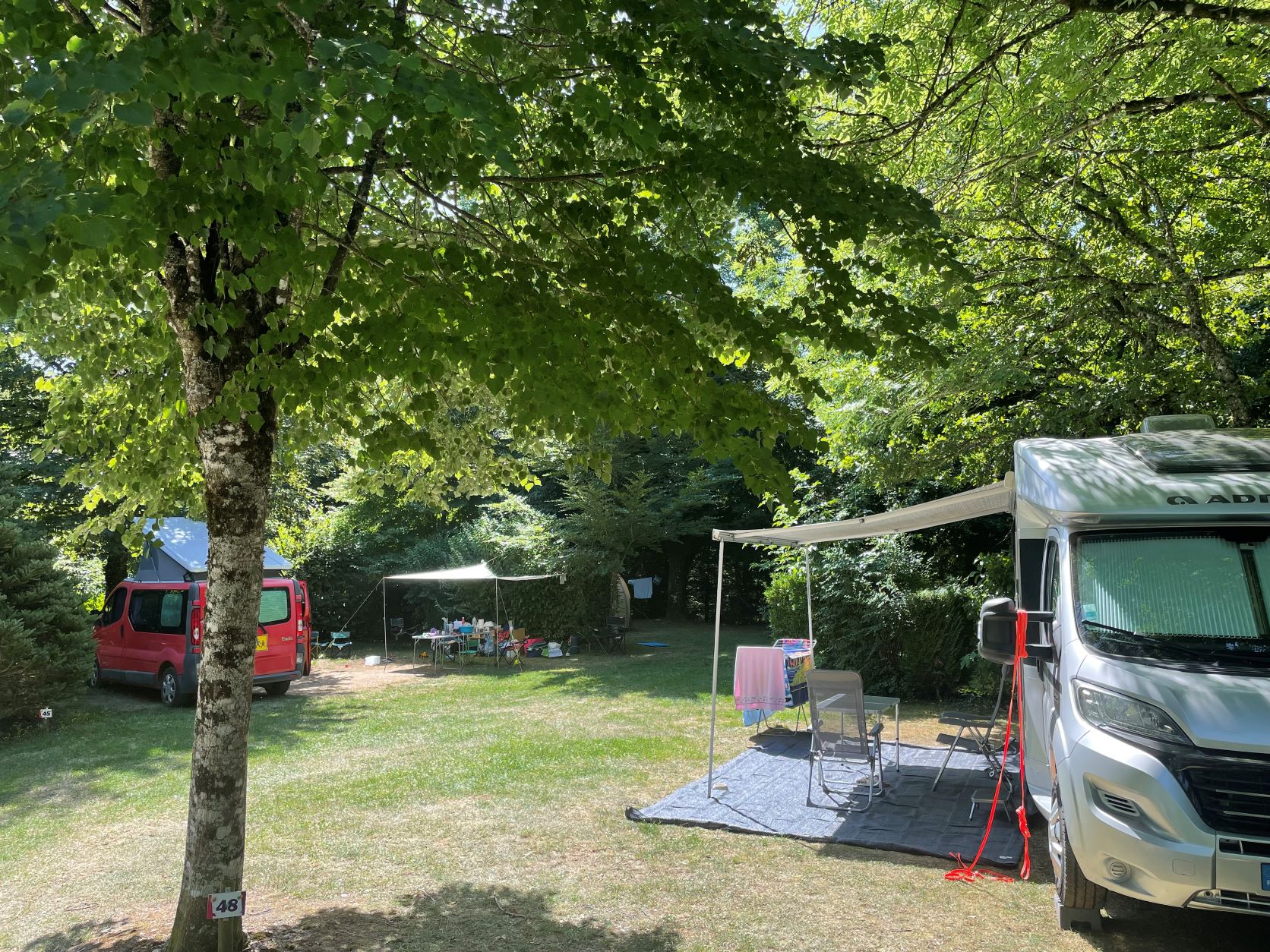 Wohnmobil und Campingbus auf einem Stellplatz im Grünen, mit Vorzelt, Tisch und Stühlen neben dem Gras.
