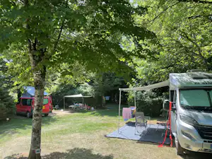Wohnmobil und Campingbus auf einem Stellplatz im Grünen, mit Vorzelt, Tisch und Stühlen neben dem Gras.
