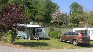 Wohnmobil auf dem Stellplatz mit Vorzelt und Tisch, daneben geparkter SUV; umgeben von Bäumen und Rasen im Campingbereich.