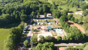 Luftaufnahme eines Campingplatzes mit Gebäuden, Stellplätzen und Wegen im Grünen, umgeben von Bäumen und Wiesen.