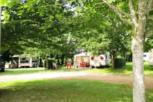 Wohnwagen und Zelte auf einem Campingplatz im Grünen, mit Gartenmöbeln und Bäumen entlang des Weges.