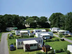 Reihen von Wohnmobilen und Mobilheimen auf einem Campingplatz, mit gepflegten Wegen, Rasenflächen und Bäumen im Hintergrund.
