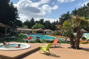 Camping-Pool mit Whirlpool, Sonnenliegen und grünen Liegestühlen, Palmen und Bungalows im Hintergrund.