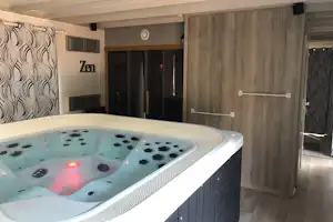 Whirlpool im Badebereich mit beleuchtetem Wasser, Holzverkleidung und Handtuchhalter, im Hintergrund Türen und Wanddekoration.