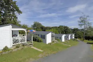 Reihen von Camping-Bungalows mit Terrasse, weißem Holzgeländer und Rasenfläche neben einem schmalen Weg.