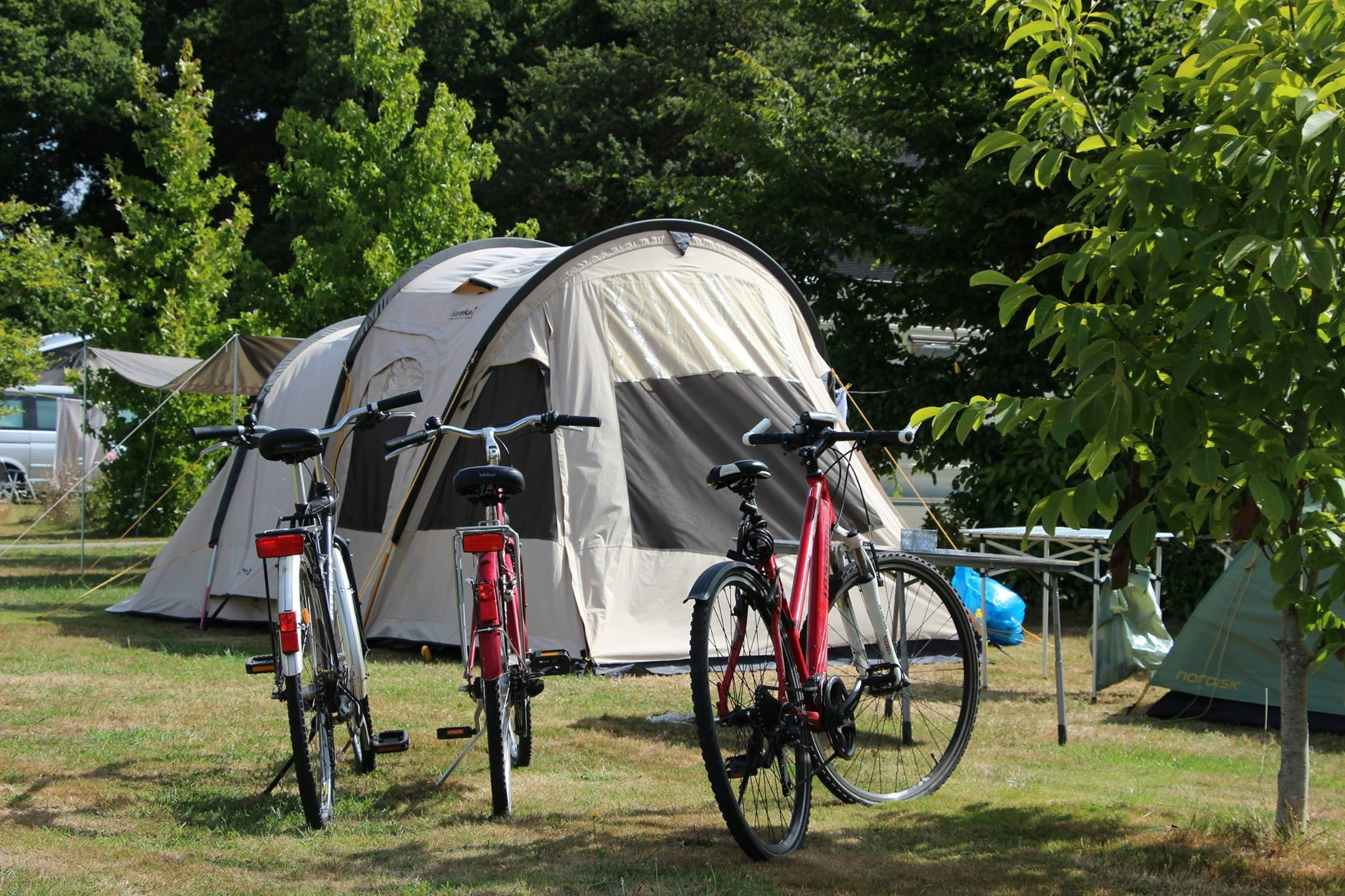 Campingzelt im Grünen, davor Fahrräder am Stellplatz, Hecke und Bäume im Hintergrund.