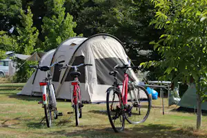 Campingzelt im Grünen, davor Fahrräder am Stellplatz, Hecke und Bäume im Hintergrund.