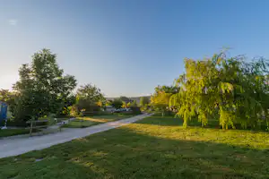 Campingweg mit gepflegtem Rasen und Bäumen, im Hintergrund Gebäude und ein offener Blick ins Tal.