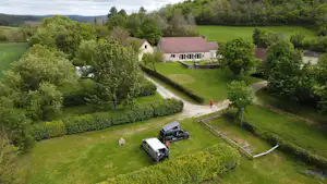 Luftaufnahme eines Campingplatzes mit Wiese, zwei Wohnwagen, Zufahrtsweg und mehreren Gebäuden im Grünen.
