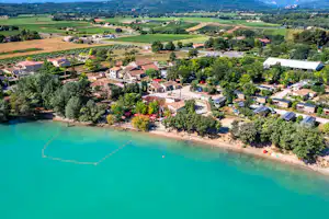 Luftaufnahme vom Campingplatz am türkisfarbenen See mit Ufer, Bäumen, Wegen und vielen Wohnmobilen sowie Zelten.