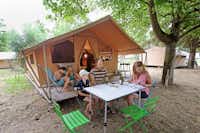 Camping de l'Ill - Colmar - Gäste sitzen vor dem Glampingzelt im Schatten der Bäume auf dem Campingplatz