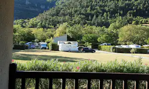 Wohnwagen und Campingfahrzeuge auf Stellplätzen in einem grünen Tal, umgeben von Bäumen und Hecken.
