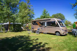 Wohnmobil mit ausklappbarer Markise und Sitzgruppe auf dem Rasen, umgeben von Bäumen und weiteren Stellplätzen.