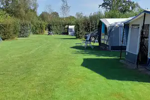 Campingplatz mit großem Rasen, zwei Zelten und Gartenmöbeln; im Hintergrund Bäume und ein weiterer Stellplatz.