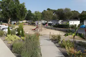 Campingplatz mit gepflasterten Wegen, Wohnwagen und Mobilheimen, Hecken und Bäumen im Hintergrund.