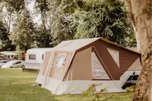 Großes Campingzelt neben einem Wohnwagen auf einer Wiese, umgeben von Bäumen und weiteren Stellplätzen.
