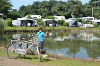 Camping De Molenhof - Angler am See mit Wohnwagen auf Stellplätzen im Hintergrund