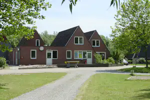Ziegelhaus mit mehreren Fenstern, Bank vor dem Eingang, Kiesweg und Bäume rundherum auf dem Campinggelände.
