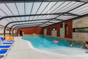 Innenpool mit blauem Wasser, Liegen am Rand und Ziegelwand im Hintergrund unter einem Glasdach.