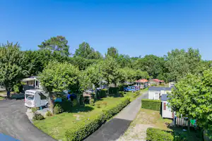 Wohnwagen und Wohnmobil auf einem Campingplatz, umgeben von Rasen, Hecken und Bäumen, mit breitem Weg zwischen den Stellplätzen.