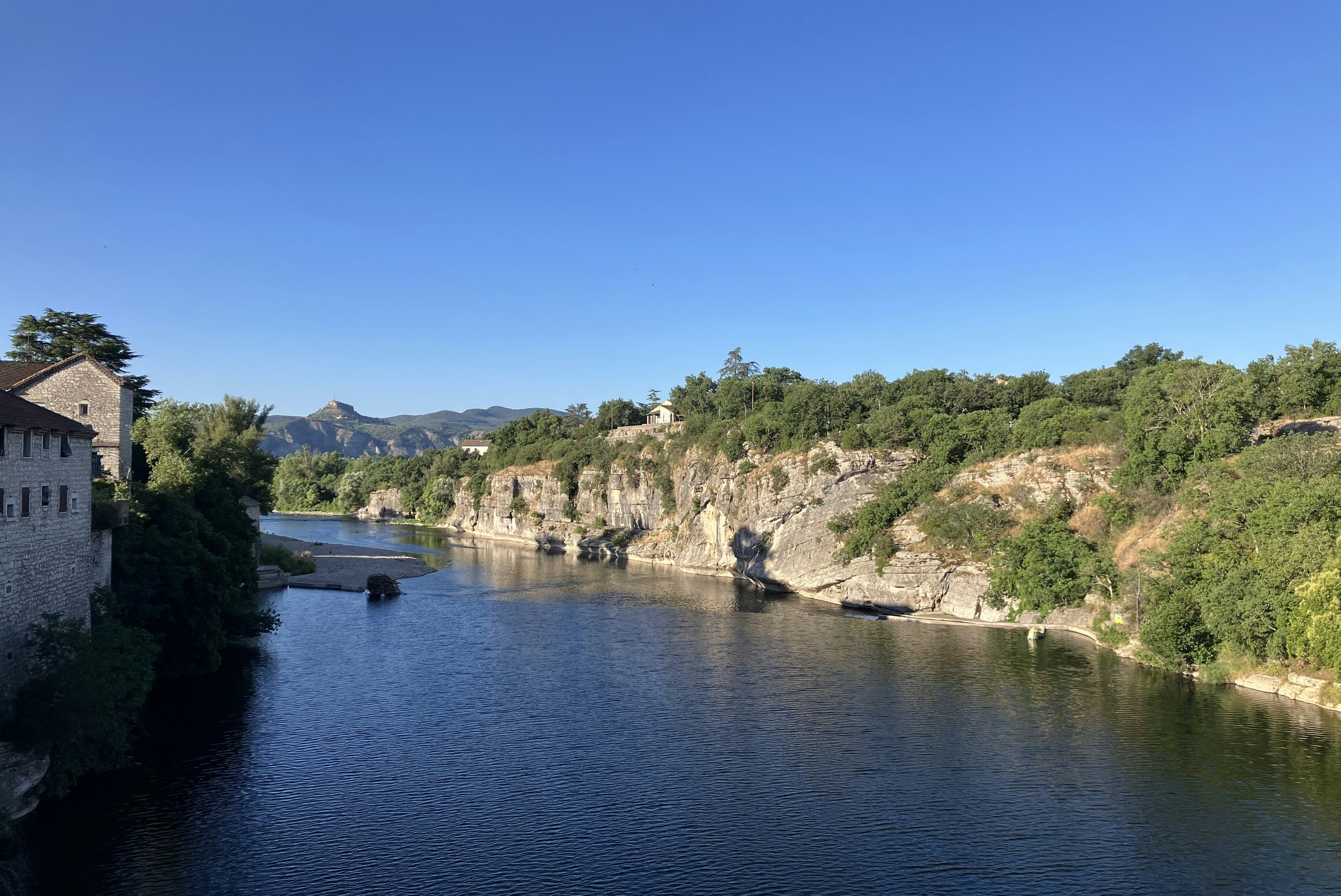 Breiter Fluss im Tal mit bewaldeten Hängen, Felswänden und einem kleinen Boot im Wasser.