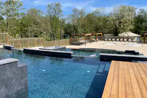 Camping-Pool mit Liegen auf der Terrasse, Holzgeländer und Zelte im Hintergrund, umgeben von Bäumen und Grün.