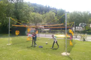 Seilnetz-Spielanlage auf dem Campingplatz, im Hintergrund Bäume und ein Gebäude mit gelben Seilen über dem Netz.
