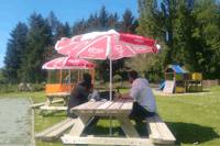 Camping de Rodaven - Trampolin und Kinderkletterburg mit Campern auf einer Bank im Vordergrund