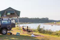 Huttopia De Roos  Camping De Roos - Gäste beim Entspannen auf ihrem Stellplatz mit Blick auf den Fluss
