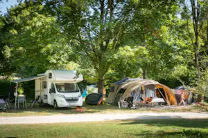 Wohnmobil und Zelte auf einem Campingplatz zwischen hohen Bäumen, mit Campingstühlen und Tisch am Stellplatz.