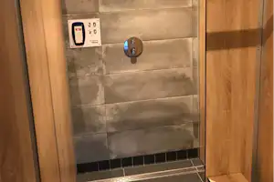 Dusche mit Wand aus Fliesen und Holzverkleidung, Duschkopf und Wandarmatur im Sanitärbereich.