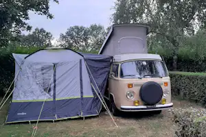 Campingzelt und Wohnmobil nebeneinander auf einem Stellplatz im Grünen, mit Bäumen im Hintergrund.