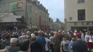 Große Menschenmenge vor Gebäuden in einer Stadt, Schilder an der Fassade und viele Besucher auf der Straße.