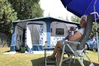 Camping De Simonshoek - Camper sitzen unter einem Sonnenschirm vor ihrem Wohnwagen