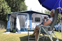 Camping De Simonshoek - Camper sitzen unter einem Sonnenschirm vor ihrem Wohnwagen