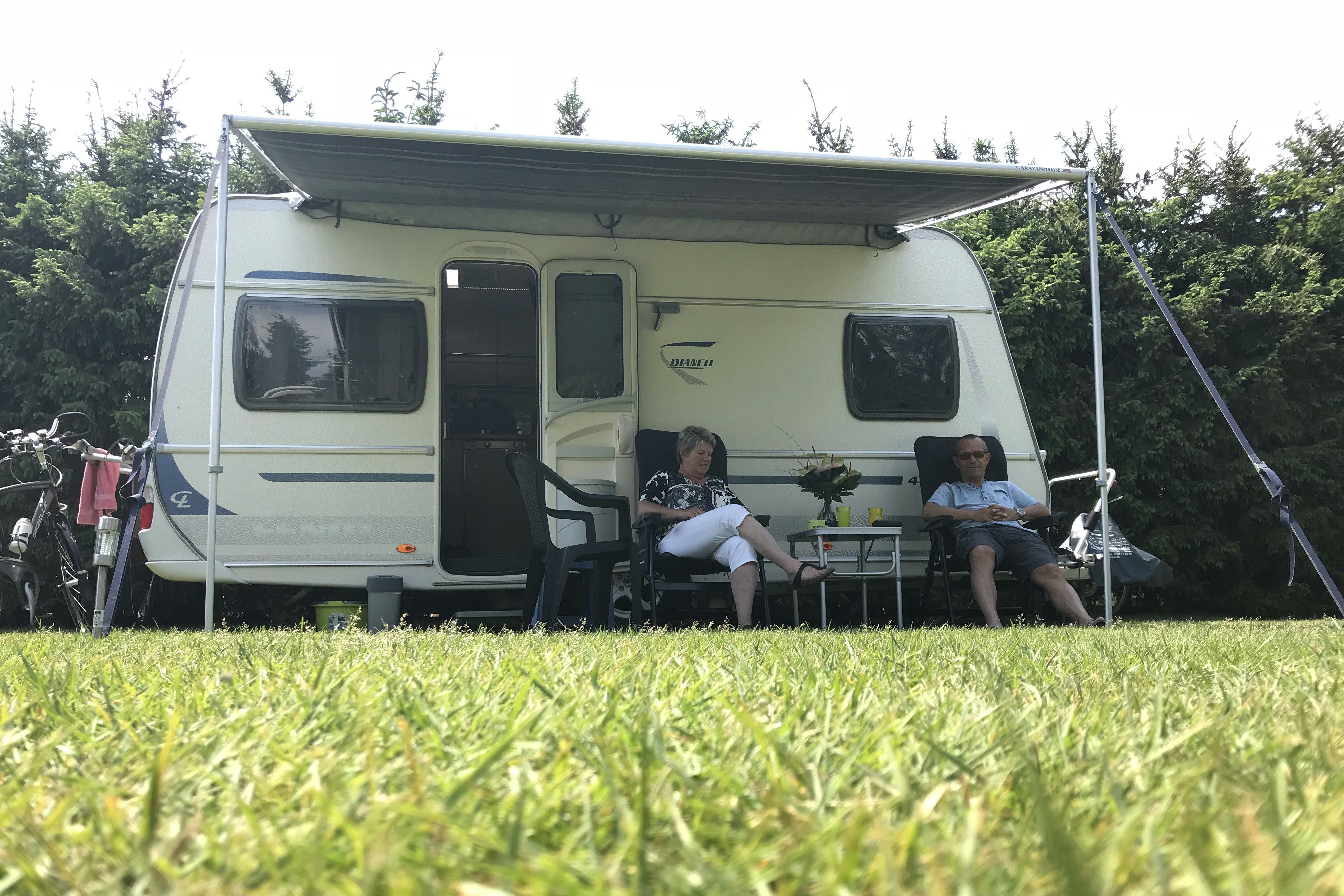 Camping De Simonshoek - Wohnwagen auf dem Campingplatz mit davor sitzenden Campern