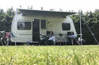 Camping De Simonshoek - Wohnwagen auf dem Campingplatz mit davor sitzenden Campern
