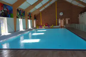 Innenpool mit blauem Wasser, bunten Kunststoffstühlen und großen Fenstern im Holz- und Ziegelraum.