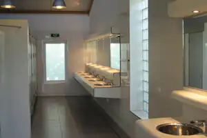 Camping-Küchenzeile mit mehreren Spülbecken, Armaturen und Fliesenwand, daneben Fenster und Türen im Sanitärbereich.