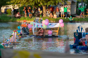 Geburtstagsdeko mit bunten Luftballons auf einem Holzboot im See, im Hintergrund Zelte und Wohnwagen am Ufer.