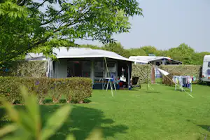 Wohnwagen auf dem Campingplatz mit Vorzelt, Stühlen und Wäscheleine im Grünen, dahinter weitere Wohnwagen und ein Auto.