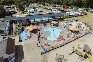 Luftaufnahme von zwei Schwimmbecken auf dem Campingplatz, umgeben von Liegen, Sonnenschirmen und Wohnmobilen.