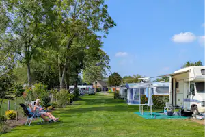 Campingplatz mit Wohnmobil und Vorzelt, gepflegtem Rasen und Sitzgelegenheiten; im Hintergrund weitere Stellplätze und Bäume.