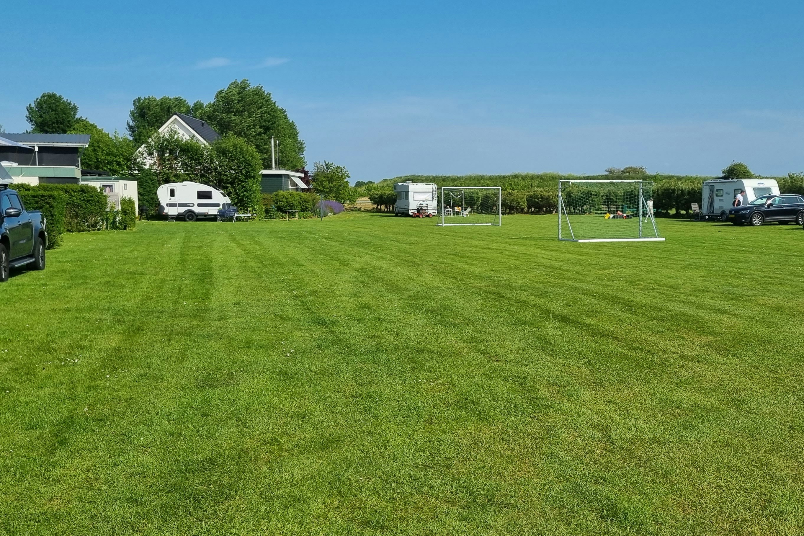 Großer Campingplatz mit gepflegtem Rasen, Wohnmobilen und Zelten, Hecken und kleinen Wegen zwischen den Stellplätzen.