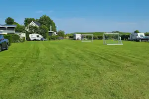 Großer Campingplatz mit gepflegtem Rasen, Wohnmobilen und Zelten, Hecken und kleinen Wegen zwischen den Stellplätzen.