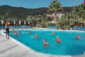 Camping Delfino - Wassergym im Swimmingpool mit Liegestühlen und Sonnenschirmen am Rand