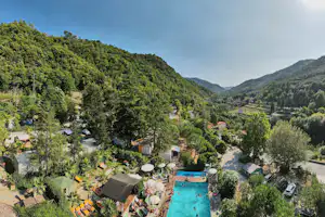 Campingplatz mit Pool inmitten von grünen Hügeln, Zelt- und Wohnwagenstellplätzen sowie Wegen zwischen Bäumen und kleinen Gebäuden.