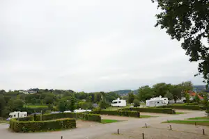 Wohnmobile auf einem Campingplatz mit grünen Hecken, gepflegten Wegen und Bäumen im Hintergrund.