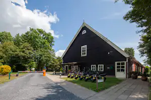 Rezeption eines Campingplatzes mit Fahrradabstellplatz vor dem Gebäude, gepflasterter Weg und Bäume im Hintergrund.